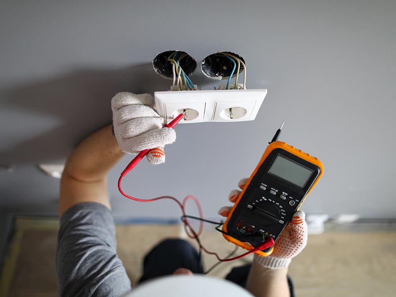 Man in hard hat and protective gloves checking wal outlet with tester